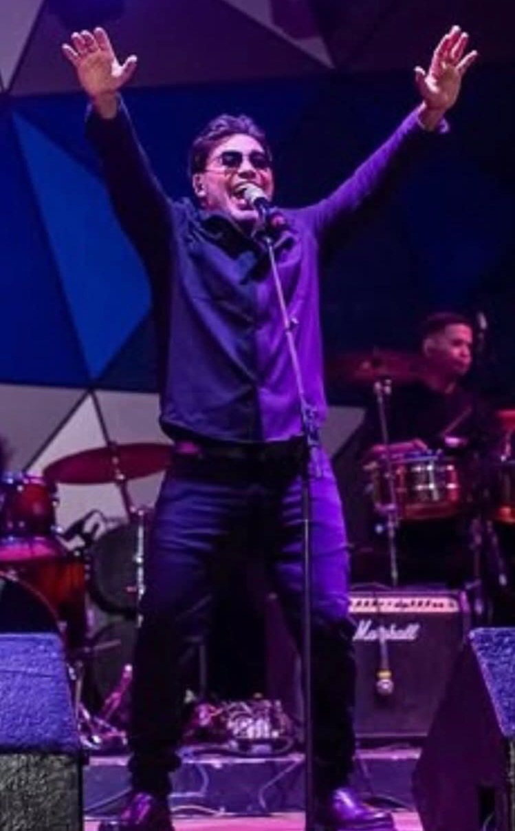 Manolín on stage with arms raised under purple lights
