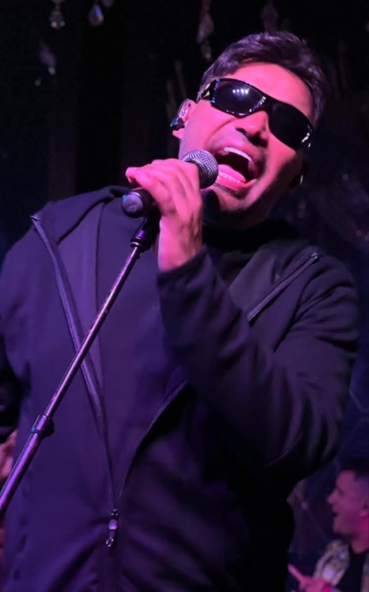 Manolín singing into a vintage microphone under warm amber light