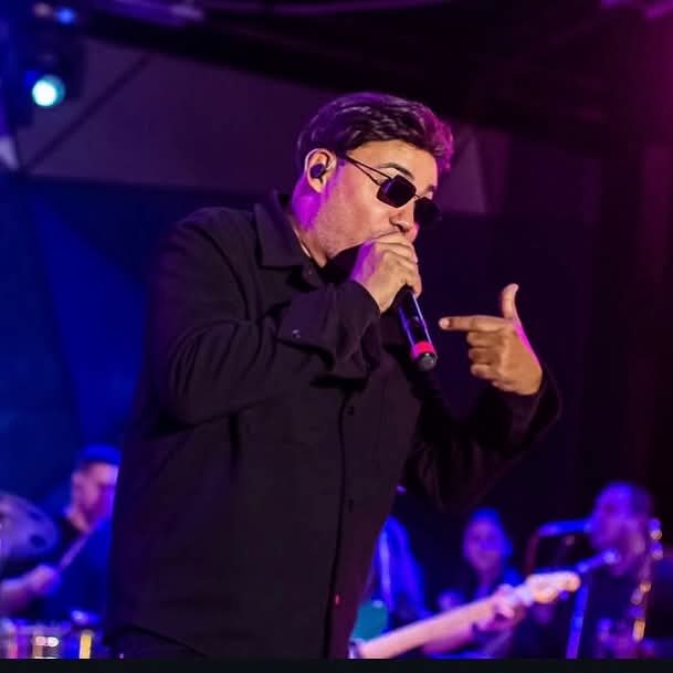 Manolín singing into a microphone with sunglasses